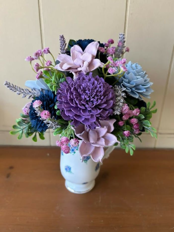 White mug with blue and purple flowers on it, green and purple filler, light purple, dk purple, light blue, and dk blue Sola Wood flowers.